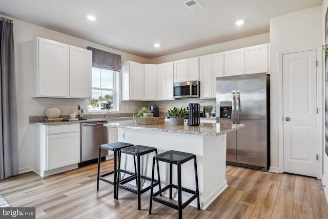 kitchen with white cabinetry, a kitchen island, stainless steel appliances, and light stone counters