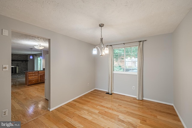 9416 Mirror Pond Dr, Fairfax, VA 22032 - empty room featuring light wood-type flooring, a textured ceiling, a fireplace, and a chandelier