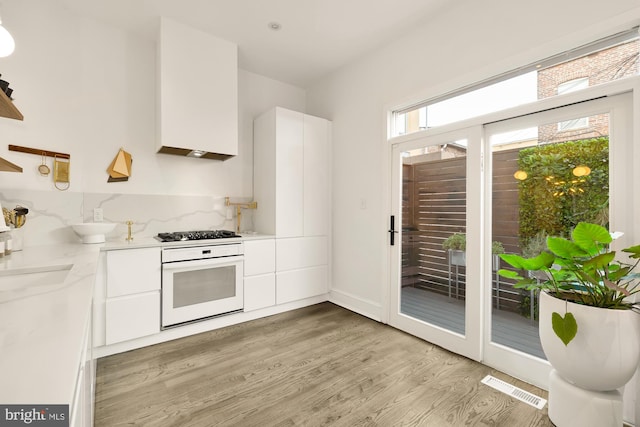 kitchen with white cabinetry, light hardwood / wood-style flooring, oven, and stainless steel gas stovetop