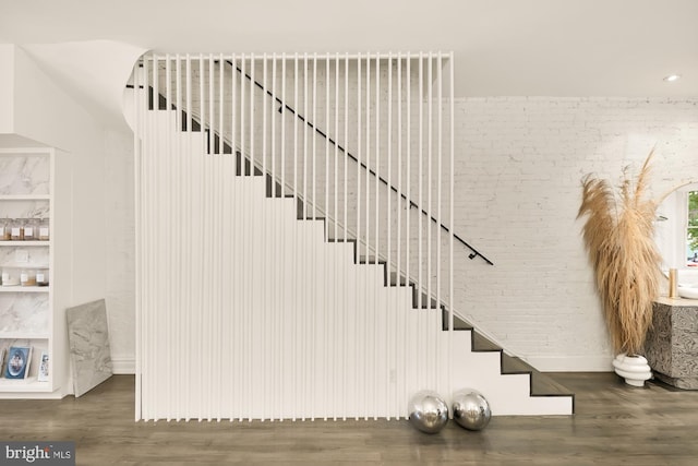 stairway with built in shelves, brick wall, and wood-type flooring