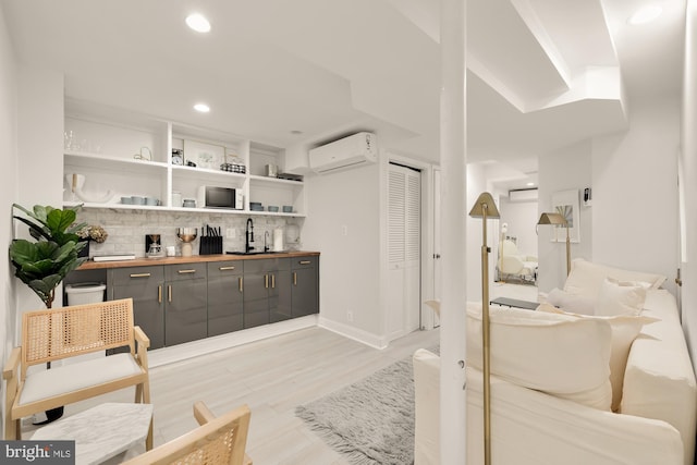 interior space with sink, gray cabinetry, a wall unit AC, light hardwood / wood-style floors, and decorative backsplash