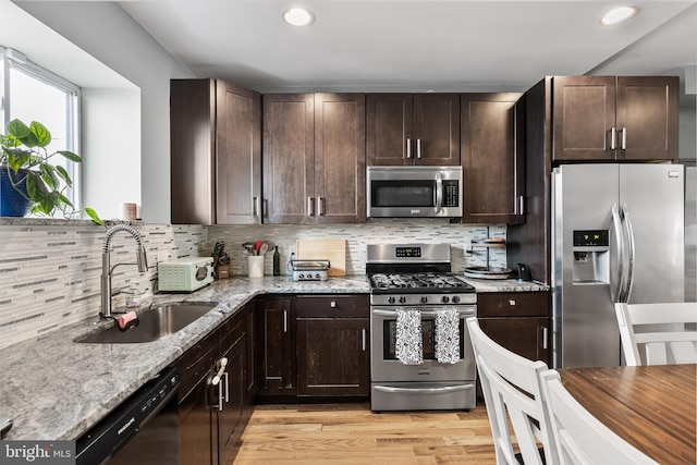 kitchen with sink, light stone counters, tasteful backsplash, light hardwood / wood-style flooring, and appliances with stainless steel finishes