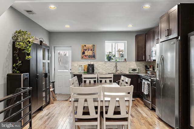 kitchen with stainless steel appliances, light hardwood / wood-style floors, dark brown cabinetry, and decorative backsplash