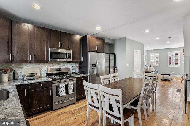 kitchen featuring tasteful backsplash, dark brown cabinets, stainless steel appliances, light stone countertops, and light hardwood / wood-style floors