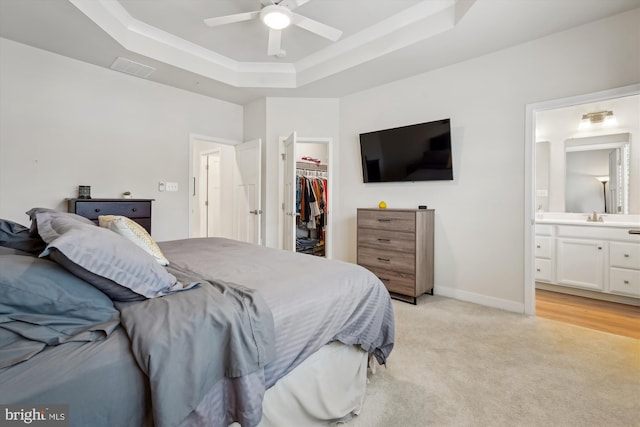 carpeted bedroom featuring ensuite bathroom, sink, a walk in closet, a raised ceiling, and a closet