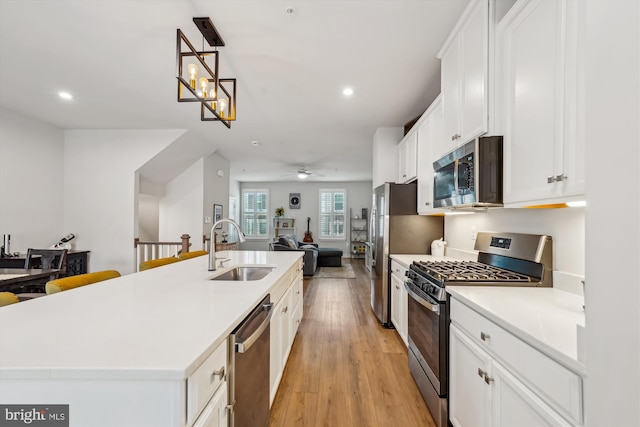 kitchen with sink, a kitchen island with sink, stainless steel appliances, white cabinets, and light wood-type flooring