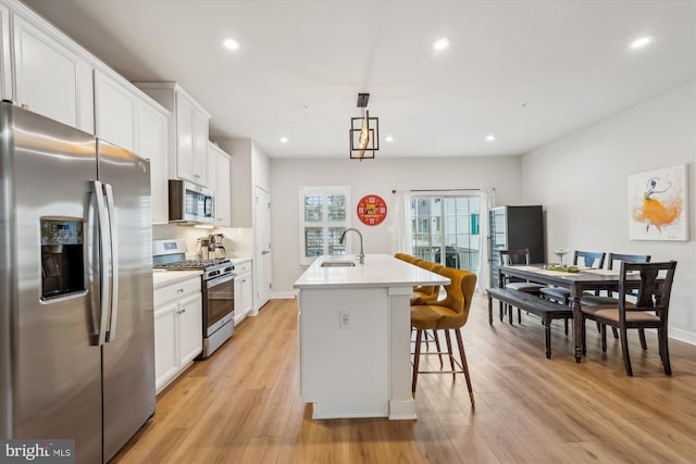 kitchen with appliances with stainless steel finishes, pendant lighting, white cabinetry, sink, and a kitchen island with sink