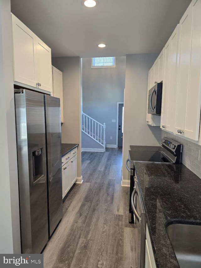 kitchen with dark stone counters, white cabinets, dark hardwood / wood-style floors, tasteful backsplash, and stainless steel appliances