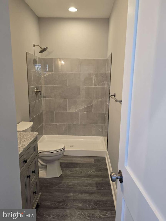 bathroom with hardwood / wood-style floors, vanity, toilet, and tiled shower