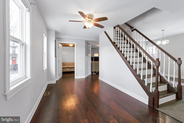 stairs with ceiling fan with notable chandelier, a healthy amount of sunlight, and wood-type flooring