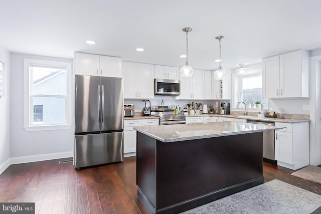 kitchen with white cabinets, decorative light fixtures, a kitchen island, and appliances with stainless steel finishes