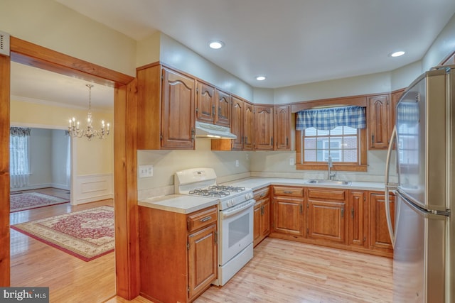 kitchen featuring gas range gas stove, sink, light hardwood / wood-style flooring, stainless steel fridge, and pendant lighting