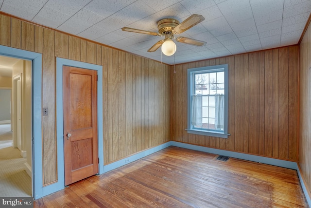 unfurnished room featuring ceiling fan, wood walls, and light hardwood / wood-style flooring