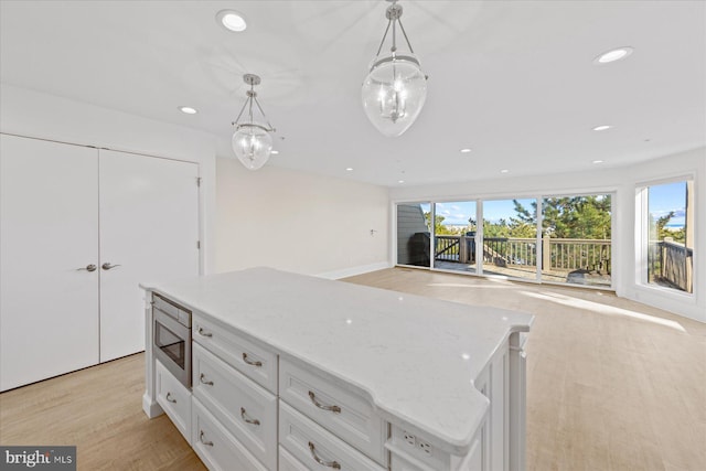 kitchen with stainless steel microwave, light hardwood / wood-style flooring, hanging light fixtures, a kitchen island, and white cabinets