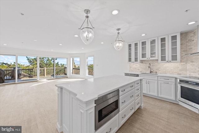 kitchen featuring stainless steel appliances, hanging light fixtures, a center island, white cabinets, and sink