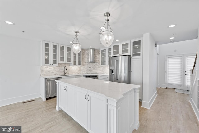 kitchen featuring stainless steel appliances, sink, white cabinets, a center island, and wall chimney range hood