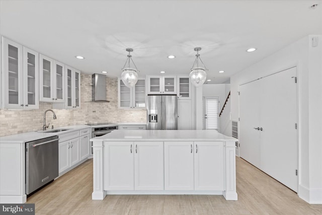 kitchen featuring hanging light fixtures, stainless steel appliances, wall chimney range hood, a kitchen island, and sink