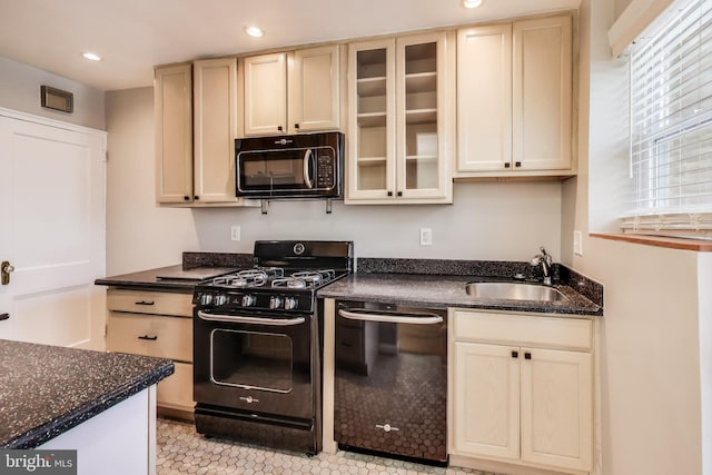 kitchen with light tile patterned flooring, dark stone counters, black appliances, cream cabinets, and sink