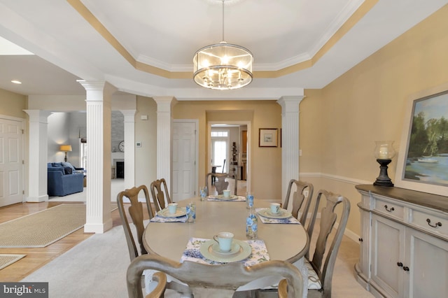 dining room with ornamental molding, a tray ceiling, light wood finished floors, decorative columns, and a chandelier