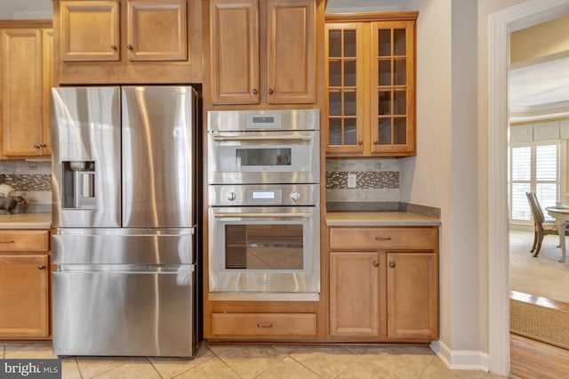 kitchen featuring backsplash, glass insert cabinets, baseboards, light countertops, and appliances with stainless steel finishes