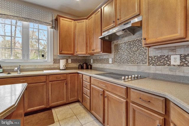 kitchen featuring under cabinet range hood, backsplash, light countertops, light tile patterned floors, and black electric stovetop