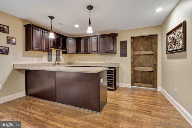 kitchen with a peninsula, dark brown cabinets, light wood-style floors, and pendant lighting