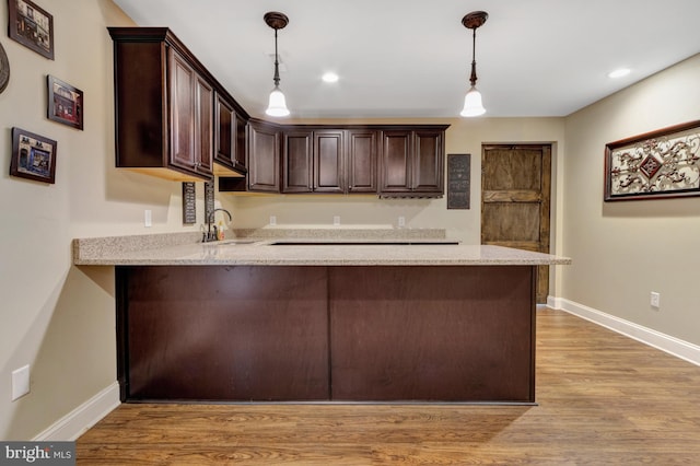 kitchen with dark brown cabinetry, a peninsula, light wood-style floors, and a sink