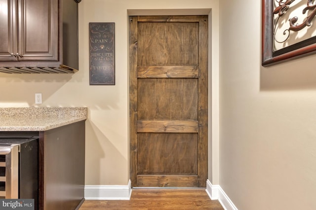 interior space featuring wood finished floors, light stone counters, beverage cooler, and baseboards