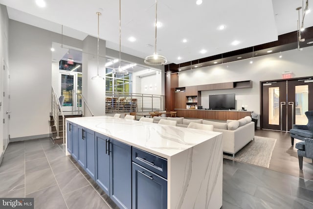 kitchen featuring light stone countertops, a towering ceiling, blue cabinets, a kitchen island, and hanging light fixtures