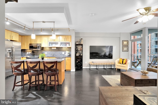 kitchen with light brown cabinetry, backsplash, stainless steel appliances, pendant lighting, and a kitchen island