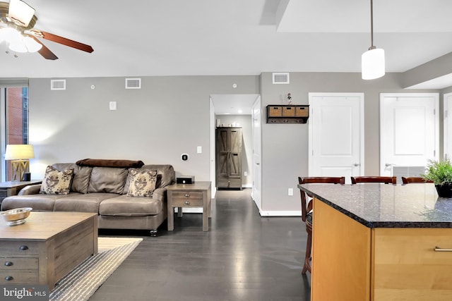 kitchen featuring dark stone countertops, ceiling fan, light brown cabinetry, and hanging light fixtures