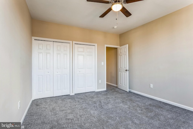 unfurnished bedroom featuring dark colored carpet, ceiling fan, and multiple closets