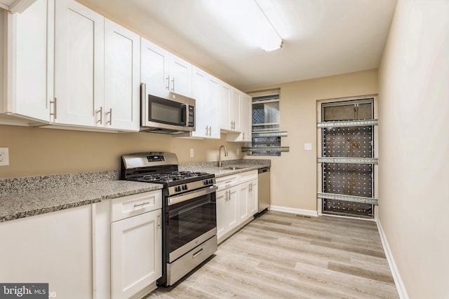 kitchen featuring white cabinets, sink, light hardwood / wood-style flooring, light stone counters, and stainless steel appliances