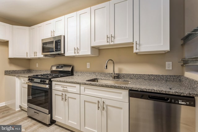 kitchen with white cabinets, sink, light stone countertops, appliances with stainless steel finishes, and light hardwood / wood-style floors