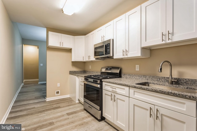 kitchen featuring sink, light wood-type flooring, light stone countertops, appliances with stainless steel finishes, and white cabinetry