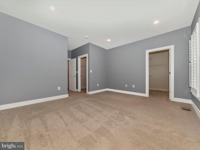 unfurnished bedroom featuring a walk in closet, a closet, and light carpet