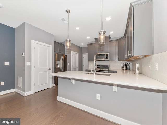 kitchen featuring stainless steel appliances, kitchen peninsula, a breakfast bar, decorative light fixtures, and backsplash