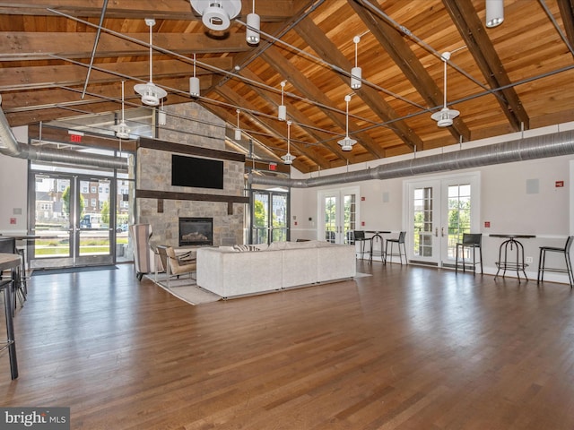 unfurnished living room featuring french doors, wooden ceiling, beam ceiling, and a stone fireplace