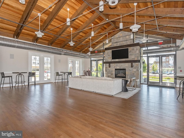 unfurnished living room featuring dark wood-type flooring, wood ceiling, beamed ceiling, and a stone fireplace