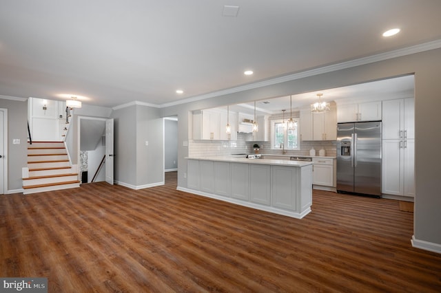 kitchen featuring kitchen peninsula, stainless steel fridge, backsplash, decorative light fixtures, and white cabinetry