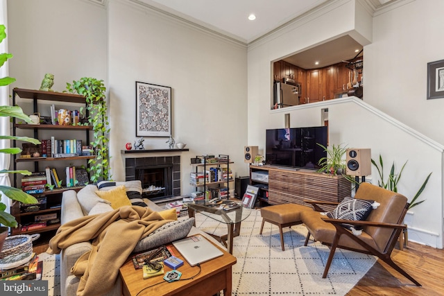 living room with light wood-type flooring, a tile fireplace, and crown molding