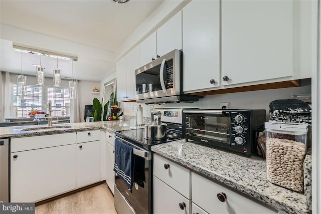 kitchen with light stone countertops, sink, appliances with stainless steel finishes, white cabinets, and light wood-type flooring