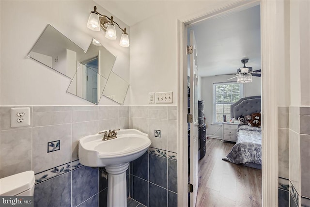 bathroom featuring wood-type flooring, toilet, tile walls, and ceiling fan