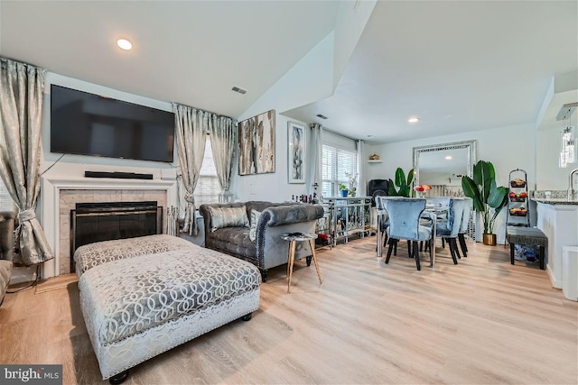 living room featuring light hardwood / wood-style floors, vaulted ceiling, and a tiled fireplace