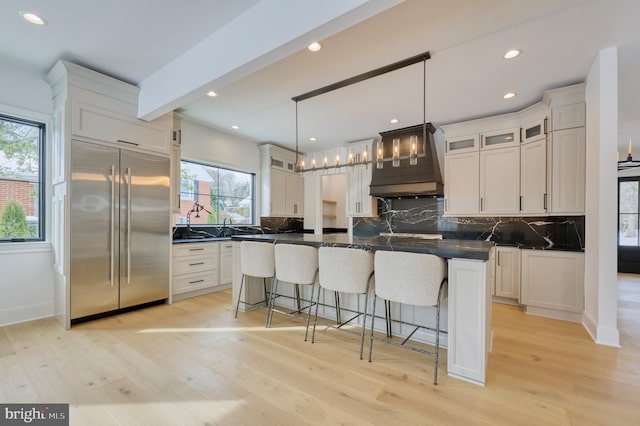 kitchen with built in fridge, custom exhaust hood, a kitchen island, and white cabinets