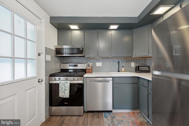 kitchen featuring gray cabinetry, backsplash, dark wood-type flooring, sink, and appliances with stainless steel finishes