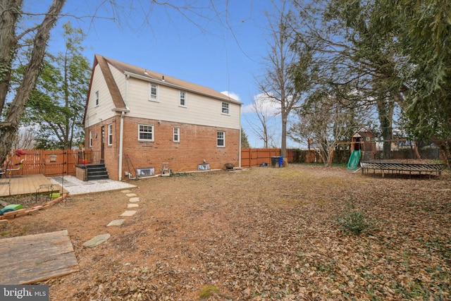 rear view of property with a trampoline, a wooden deck, and a playground