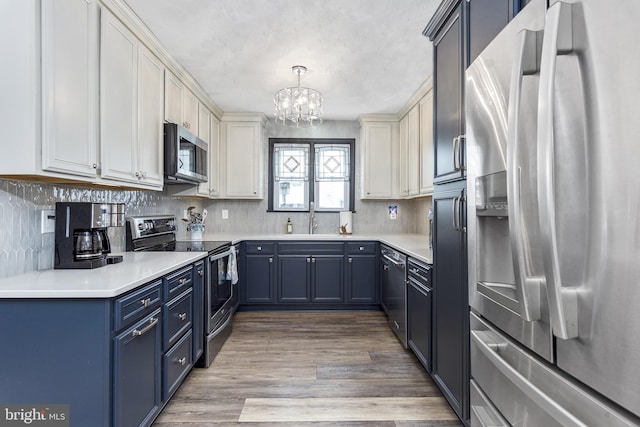 kitchen with decorative light fixtures, light countertops, appliances with stainless steel finishes, white cabinets, and a sink