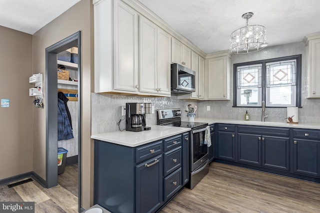 kitchen with appliances with stainless steel finishes, light countertops, light wood-type flooring, blue cabinetry, and white cabinetry