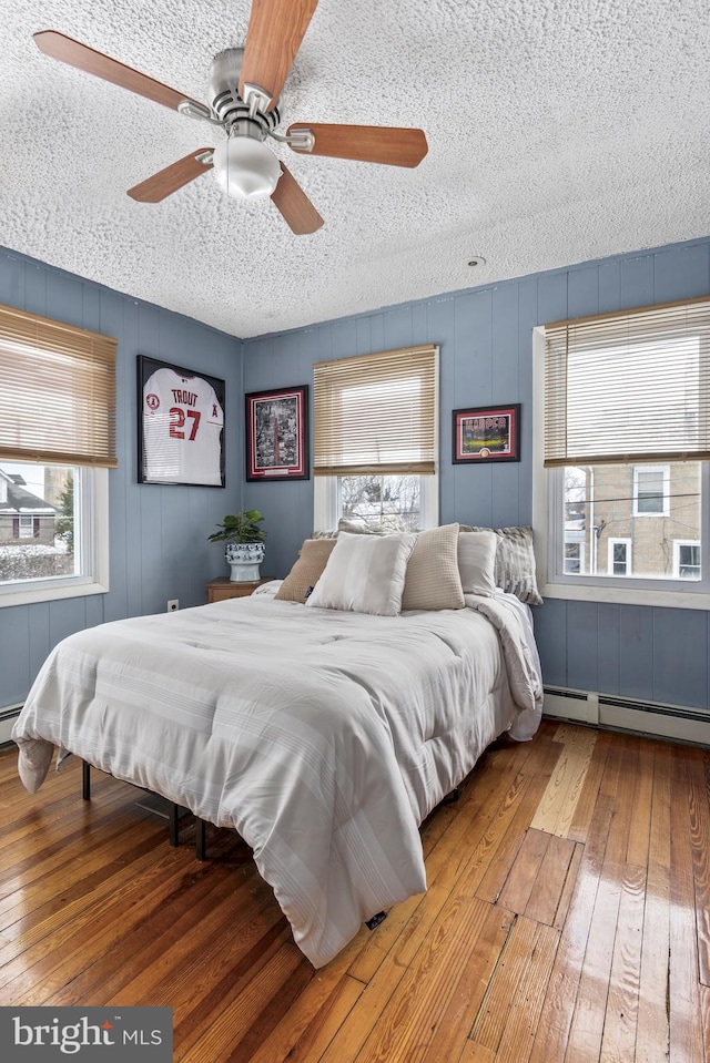 bedroom featuring a ceiling fan, a baseboard radiator, a textured ceiling, and wood finished floors